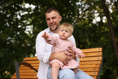 Photo of Smiling dad and his newborn girl on bench outdoors. Happy Father's Day