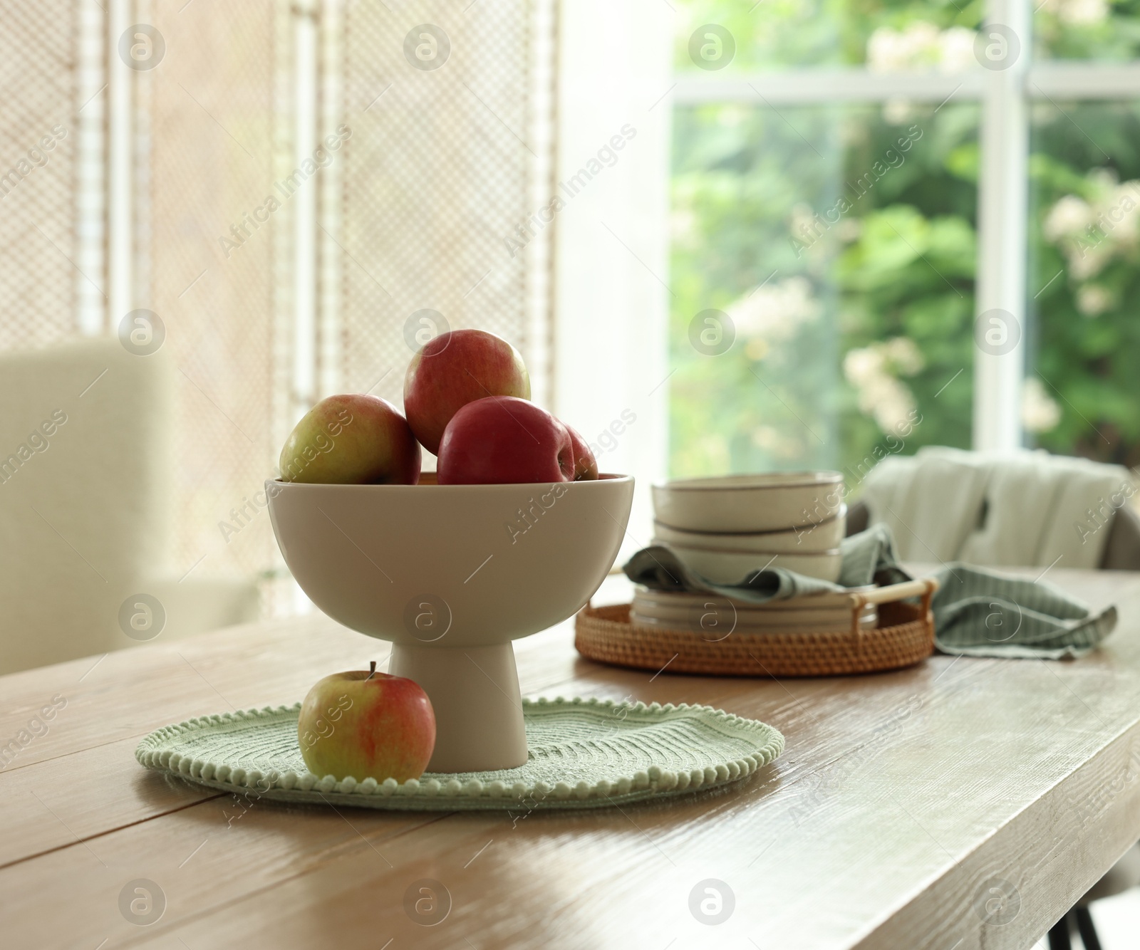 Apples and clean dishware on wooden table in dining room Photo of Apples and clean dishware on wooden table in dining room