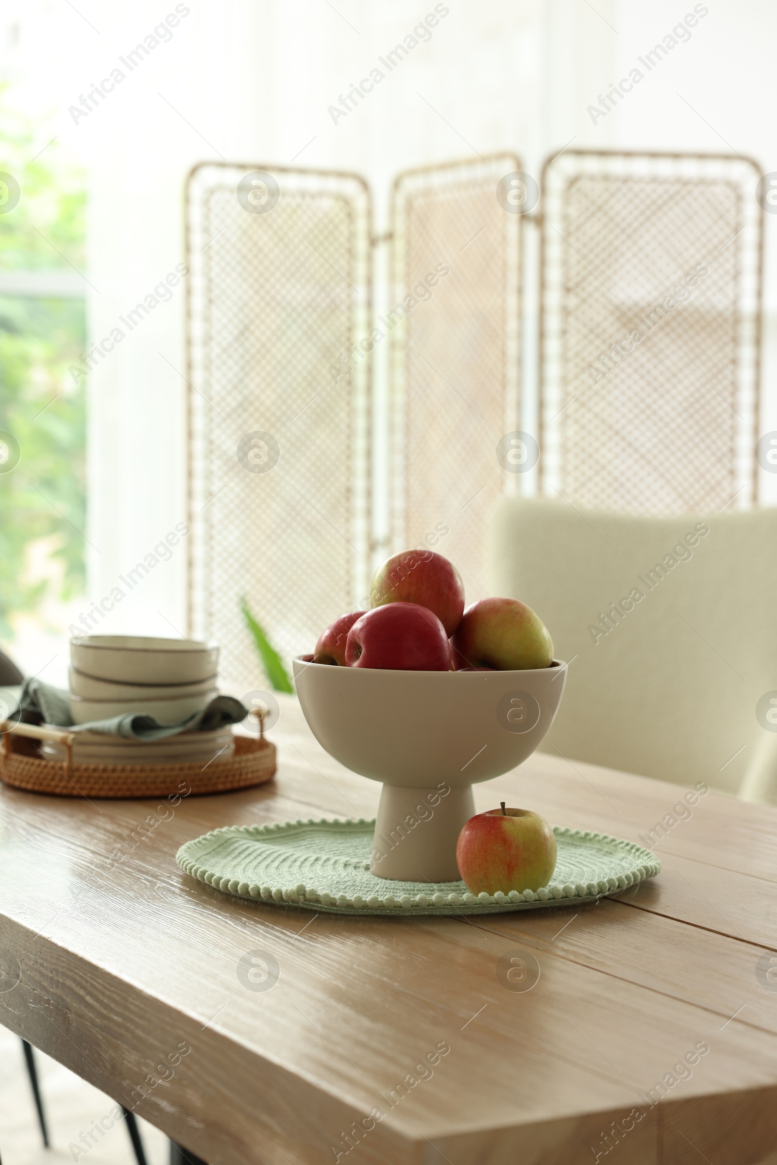 Apples and clean dishware on wooden table in dining room Photo of Apples and clean dishware on wooden table in dining room
