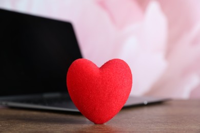 Photo of Decorative heart and laptop on wooden table, closeup. Online dating site