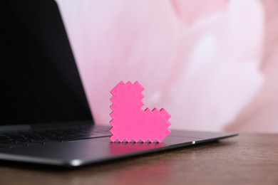 Photo of Decorative heart and laptop on wooden table, closeup. Online dating site