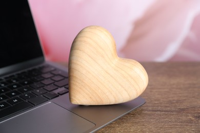 Photo of Wooden heart and laptop on table, closeup. Online dating site