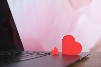 Photo of Decorative hearts and laptop on wooden table, closeup. Online dating site