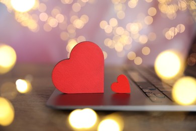 Photo of Online dating site. Decorative hearts and laptop on wooden table against blurred lights, closeup. Bokeh effect