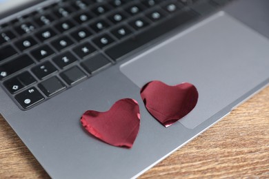 Photo of Decorative hearts and laptop on wooden table, closeup. Online dating site