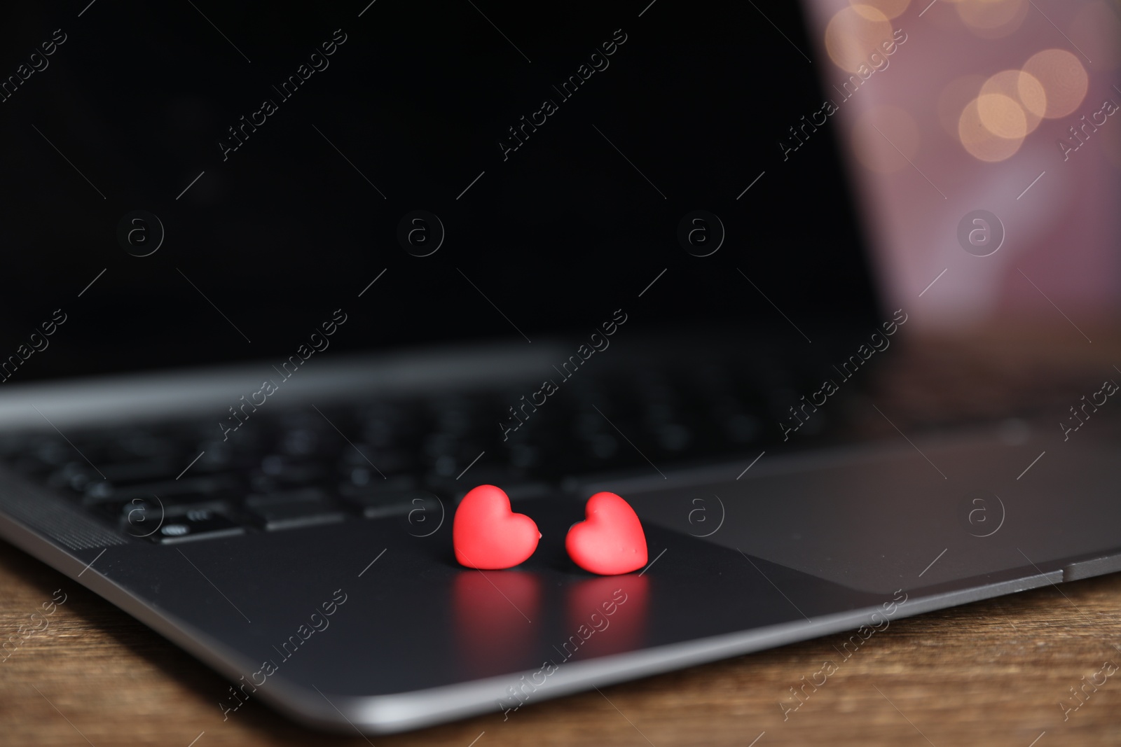 Online dating site. Decorative hearts and laptop on wooden table against blurred lights, closeup. Bokeh effect Photo of Online dating site. Decorative hearts and laptop on wooden table against blurred lights, closeup. Bokeh effect