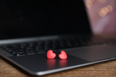 Photo of Online dating site. Decorative hearts and laptop on wooden table against blurred lights, closeup. Bokeh effect
