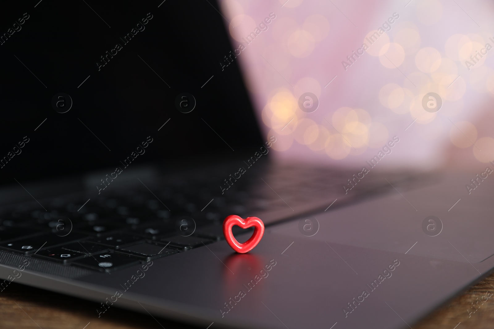 Online dating site. Decorative heart and laptop on table against blurred lights, closeup. Bokeh effect Photo of Online dating site. Decorative heart and laptop on table against blurred lights, closeup. Bokeh effect