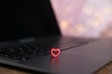Photo of Online dating site. Decorative heart and laptop on table against blurred lights, closeup. Bokeh effect