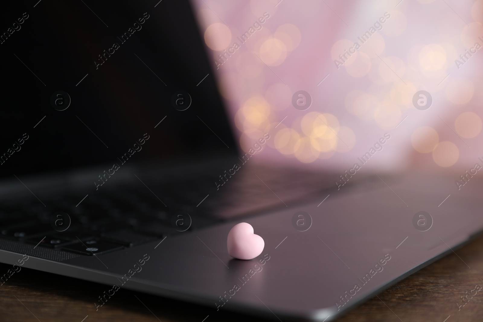 Photo of Online dating site. Decorative heart and laptop on table against blurred lights, closeup. Bokeh effect