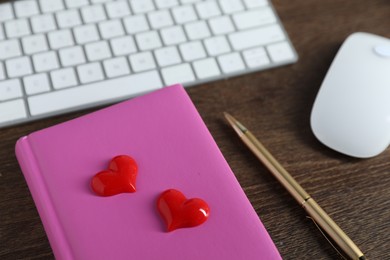 Photo of Decorative hearts, computer keyboard, mouse, notebook and pen on wooden table, closeup. Online dating site