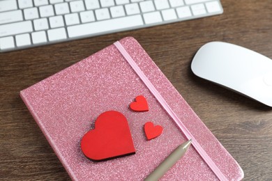 Photo of Decorative hearts, computer keyboard, mouse, notebook and pen on wooden table, above view. Online dating site