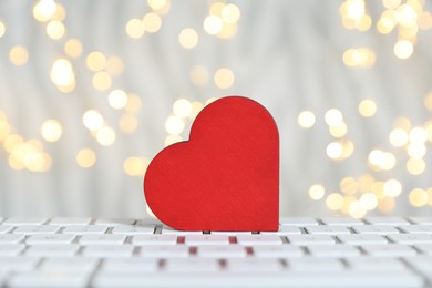 Photo of Online dating site. Decorative heart on computer keyboard against blurred lights, closeup. Bokeh effect