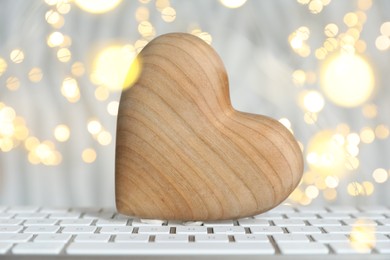 Photo of Online dating site. Wooden heart on computer keyboard against blurred lights, closeup. Bokeh effect