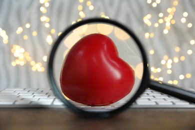 Photo of Decorative heart, computer keyboard and magnifying glass against blurred lights, bokeh effect. Online dating site