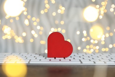 Photo of Decorative heart and computer keyboard on table against blurred lights, bokeh effect. Online dating site