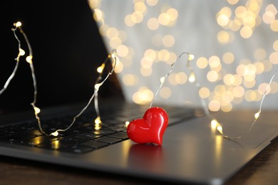 Photo of Online dating site. Decorative heart and laptop on table against blurred lights, closeup. Bokeh effect