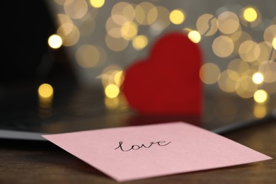 Photo of Online dating site. Sticky note with word Love, decorative heart and laptop on table, closeup. Bokeh effect