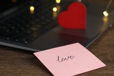 Photo of Sticky note with word Love, decorative heart and laptop on wooden table, closeup. Online dating site