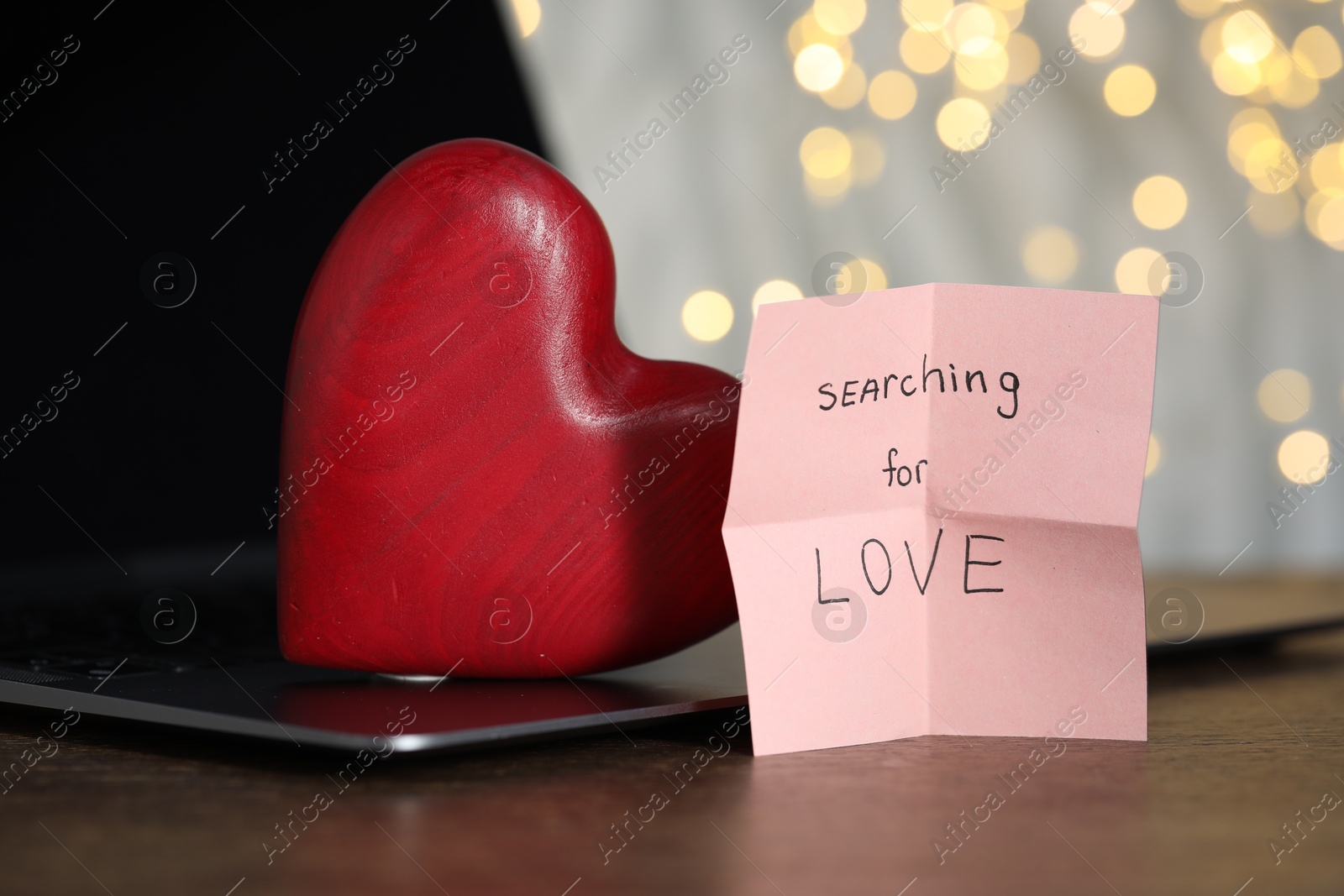 Online dating site. Sticky note with text Searching For Love, decorative heart and laptop on wooden table, closeup. Bokeh effect Photo of Online dating site. Sticky note with text Searching For Love, decorative heart and laptop on wooden table, closeup. Bokeh effect