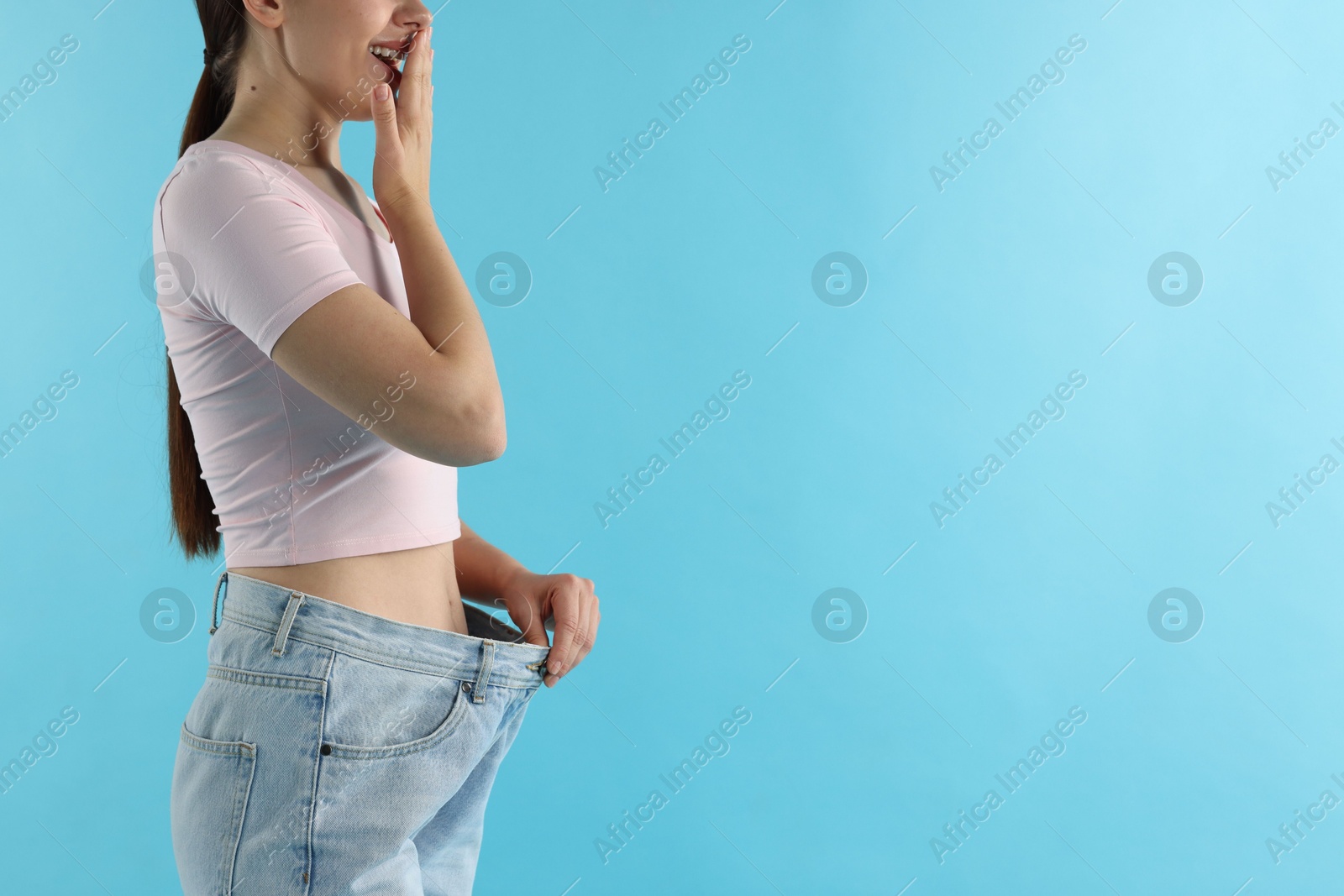 Woman wearing old jeans after weight loss on light blue background, closeup. Space for text Photo of Woman wearing old jeans after weight loss on light blue background, closeup. Space for text
