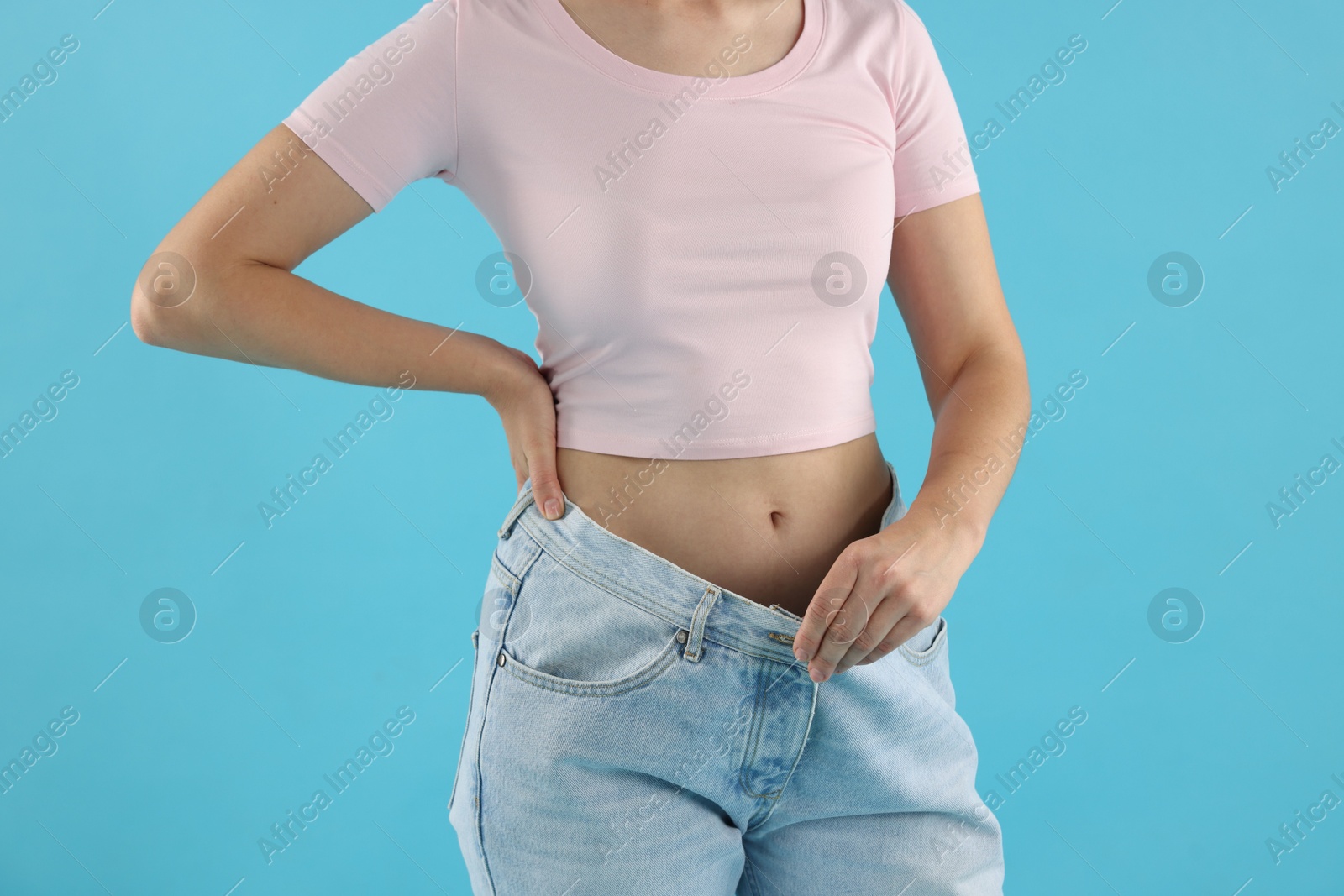 Woman wearing old jeans after weight loss on light blue background, closeup Photo of Woman wearing old jeans after weight loss on light blue background, closeup