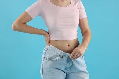 Photo of Woman wearing old jeans after weight loss on light blue background, closeup