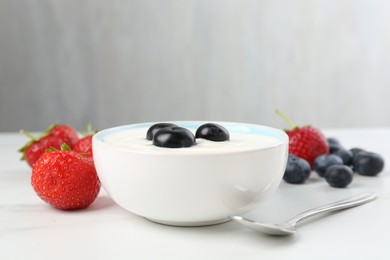 Photo of Tasty yoghurt with blueberries and strawberries in bowl on white marble table, closeup