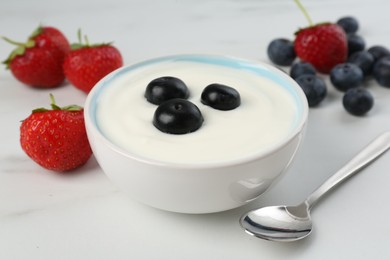 Photo of Tasty yoghurt with blueberries and strawberries in bowl on white marble table, closeup