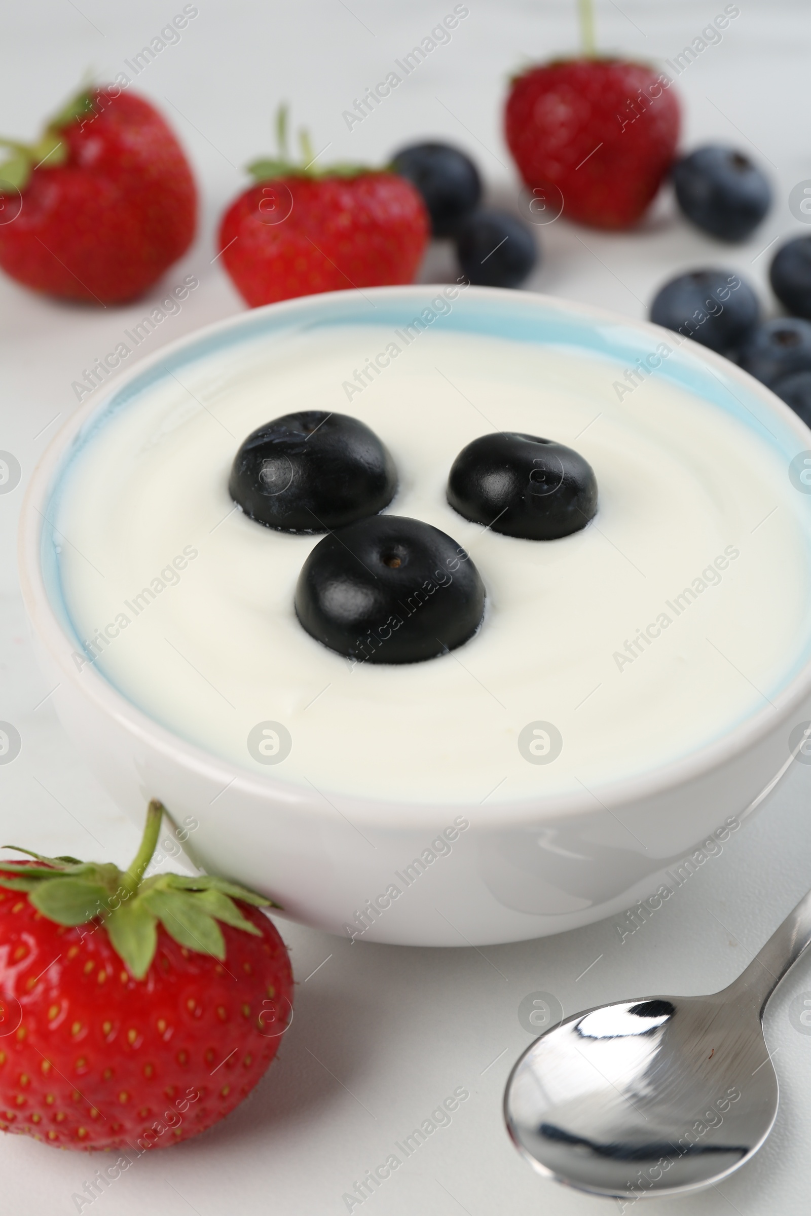 Photo of Tasty yoghurt with blueberries and strawberries in bowl on white table, closeup