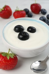 Photo of Tasty yoghurt with blueberries and strawberries in bowl on white table, closeup