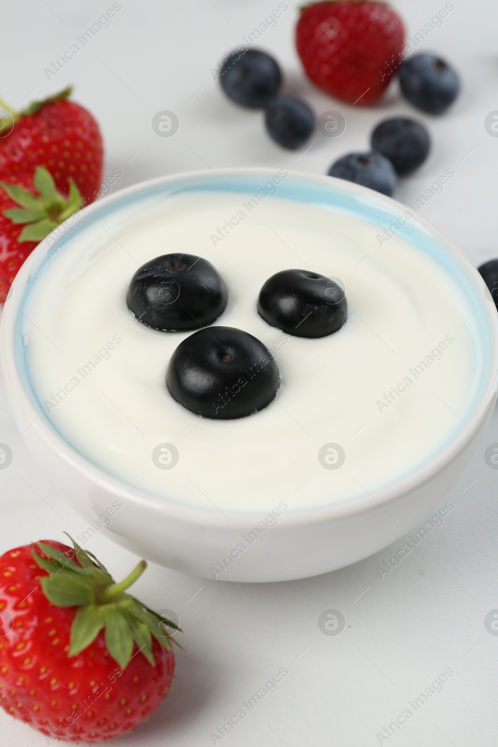 Tasty yoghurt with blueberries and strawberries in bowl on white table, closeup Photo of Tasty yoghurt with blueberries and strawberries in bowl on white table, closeup