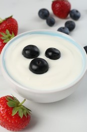 Photo of Tasty yoghurt with blueberries and strawberries in bowl on white table, closeup