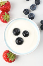 Photo of Tasty yoghurt with blueberries and strawberries in bowl on white table, flat lay