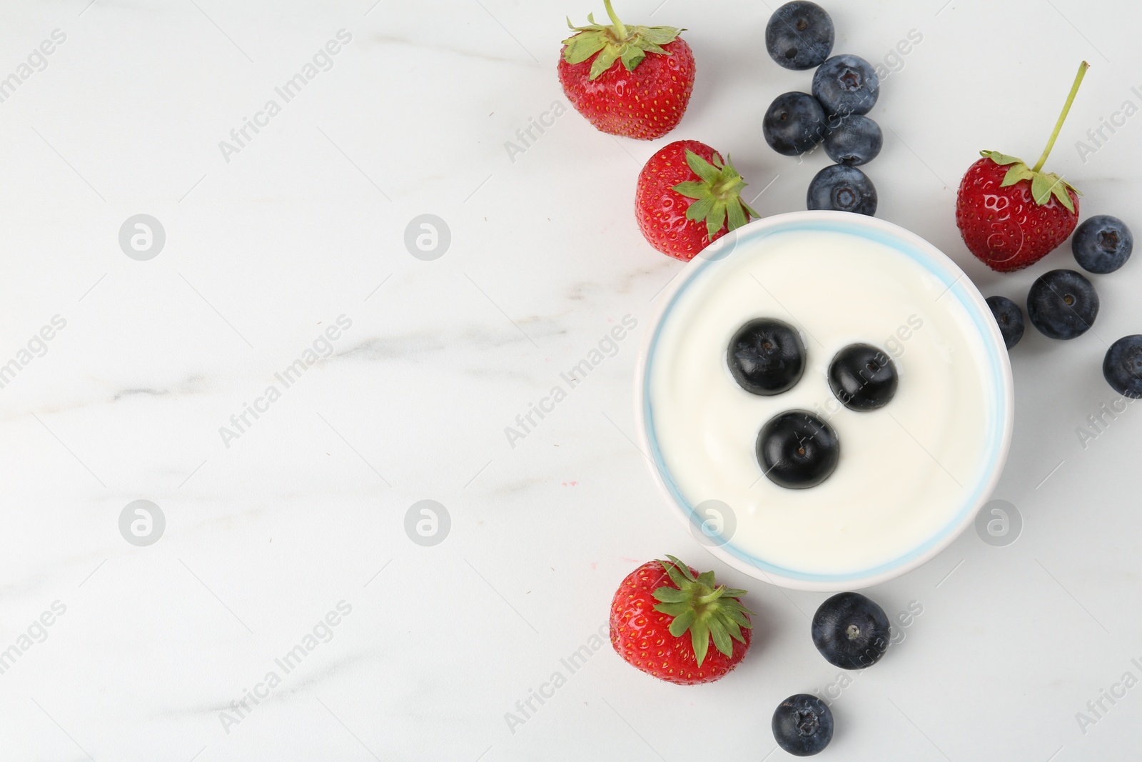 Photo of Tasty yoghurt with blueberries and strawberries in bowl on white marble table, flat lay. Space for text