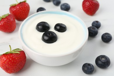 Photo of Tasty yoghurt with blueberries and strawberries in bowl on white table, closeup