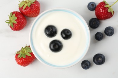 Photo of Tasty yoghurt with blueberries and strawberries in bowl on white marble table, flat lay