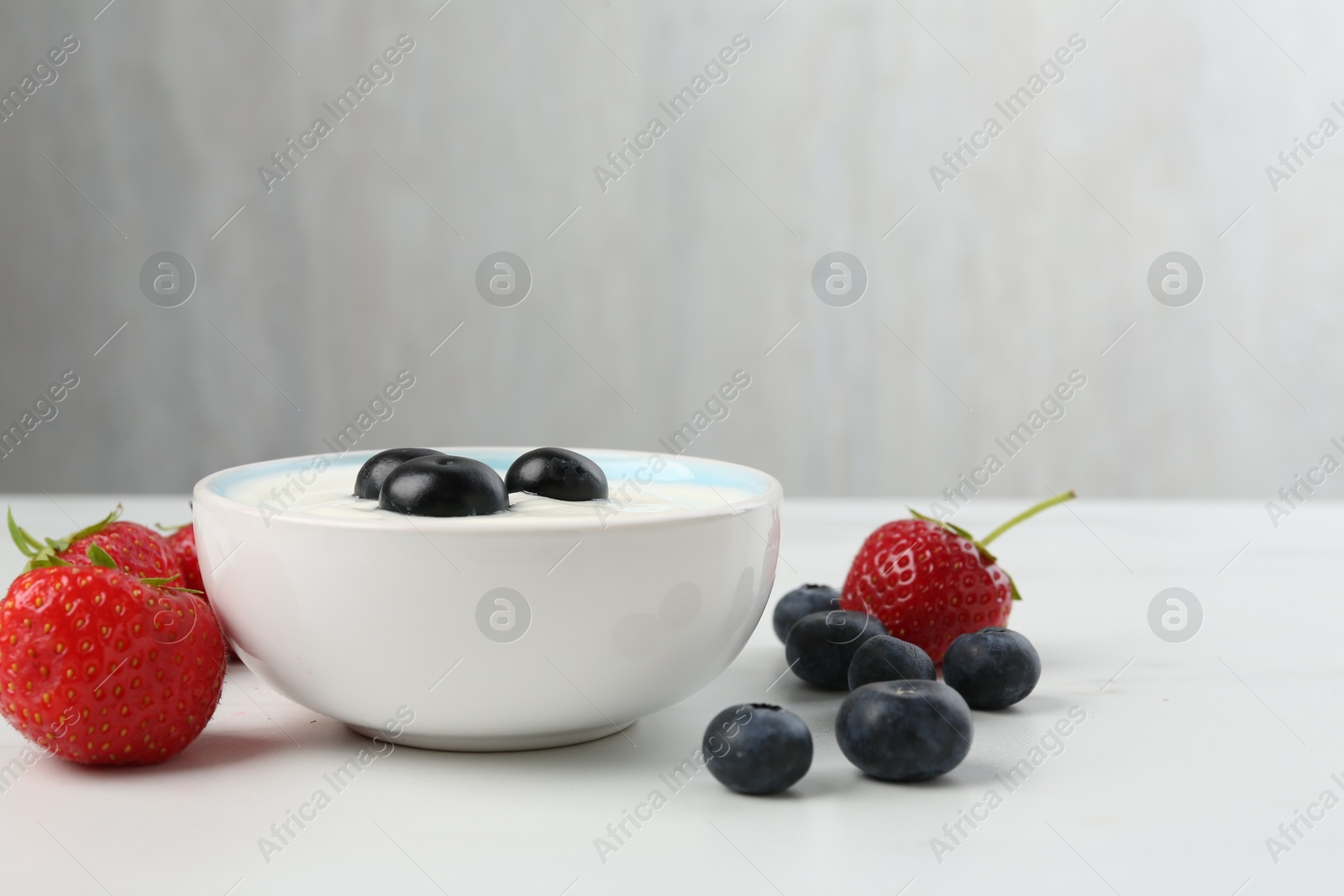 Photo of Tasty yoghurt with blueberries and strawberries in bowl on white marble table, closeup. Space for text