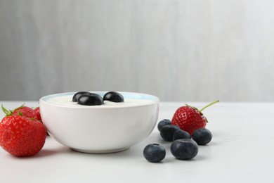 Photo of Tasty yoghurt with blueberries and strawberries in bowl on white marble table, closeup. Space for text