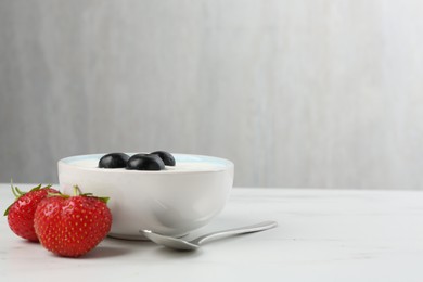 Photo of Tasty yoghurt with blueberries and strawberries in bowl on white marble table, closeup. Space for text