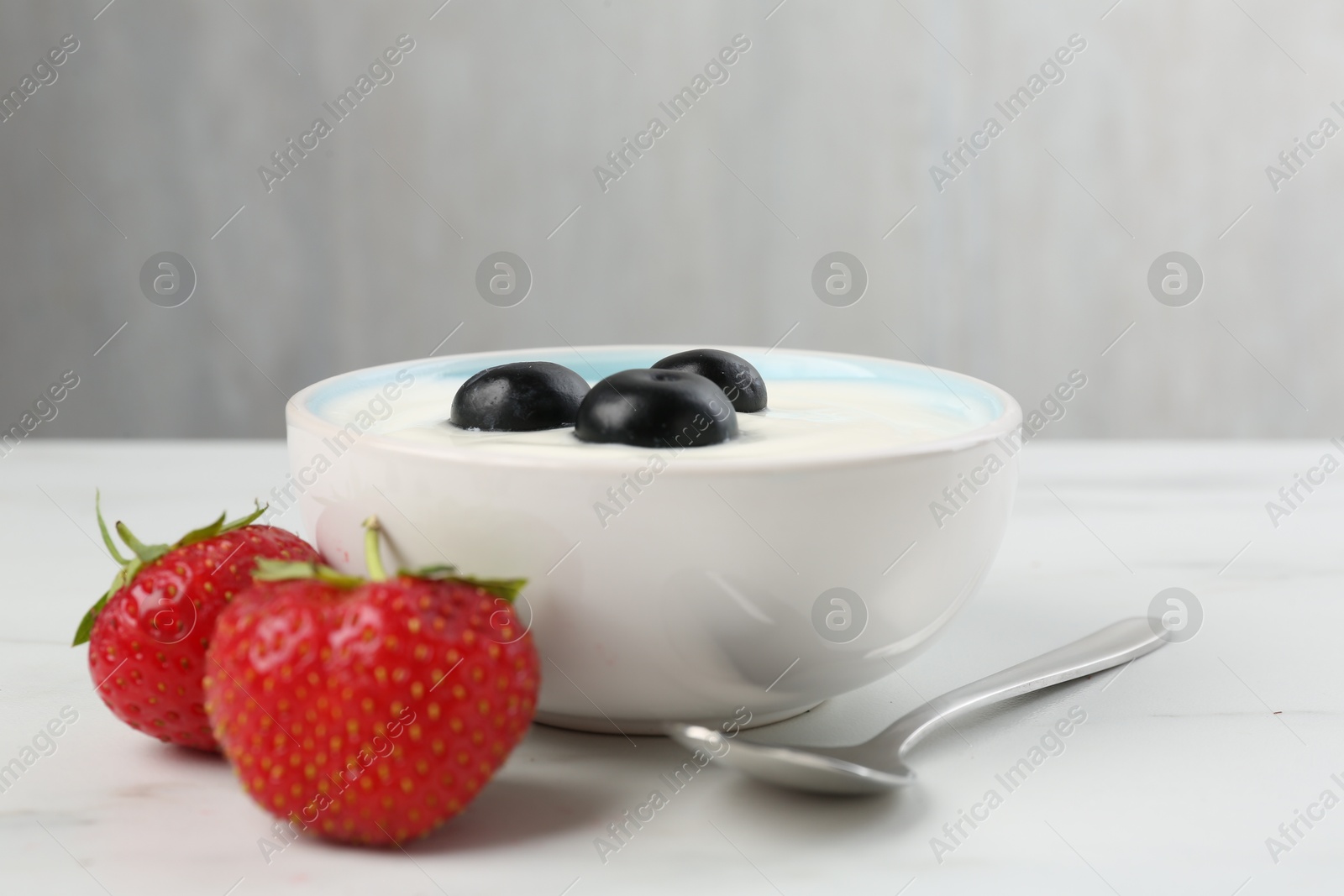 Photo of Tasty yoghurt with blueberries and strawberries in bowl on white marble table, closeup