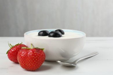 Photo of Tasty yoghurt with blueberries and strawberries in bowl on white marble table, closeup