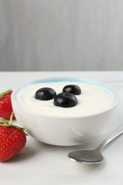 Photo of Tasty yoghurt with blueberries and strawberries in bowl on white marble table, closeup