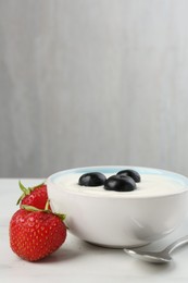 Photo of Tasty yoghurt with blueberries and strawberries in bowl on white marble table, closeup. Space for text