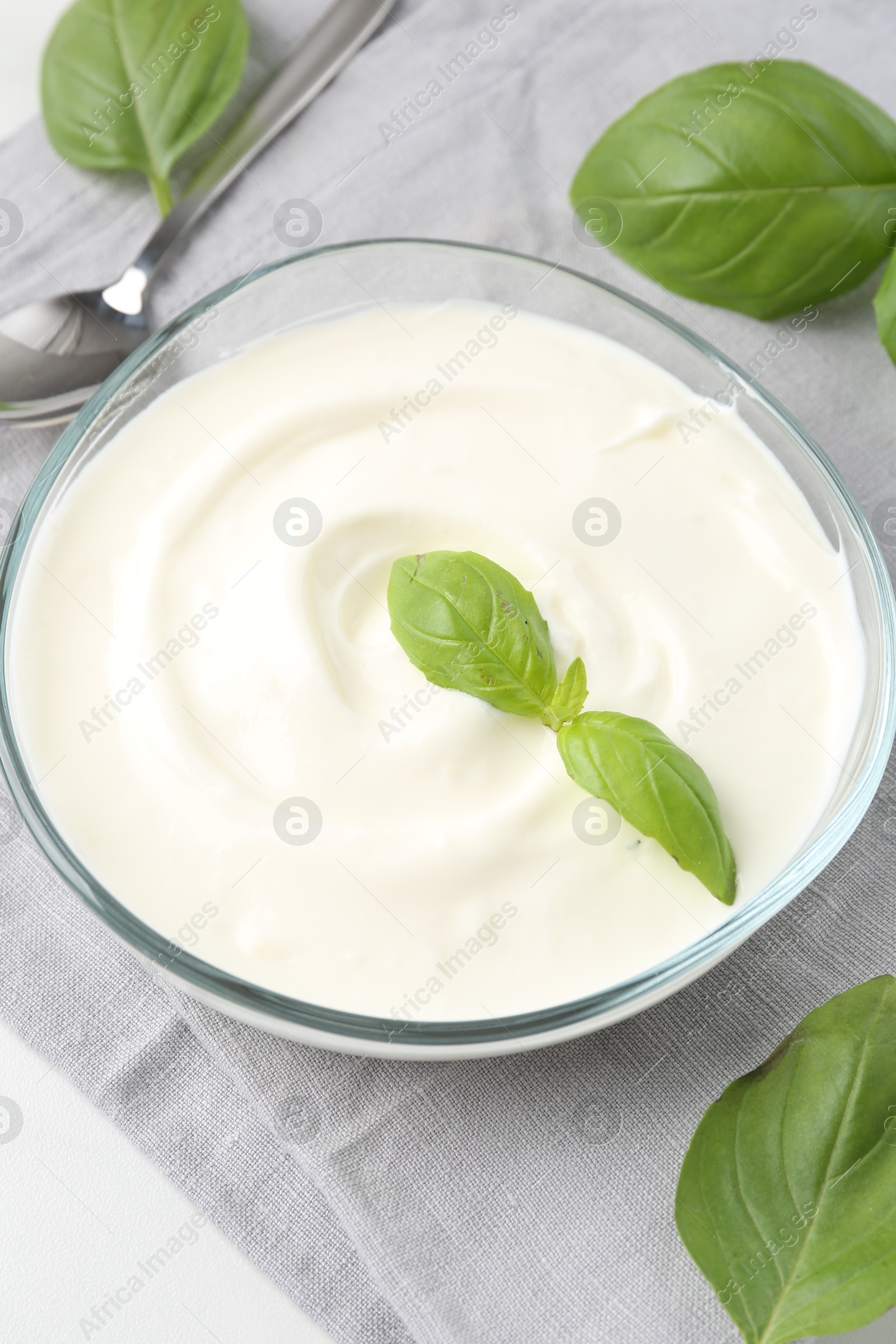 Tasty yoghurt with basil in bowl on white table, closeup Photo of Tasty yoghurt with basil in bowl on white table, closeup