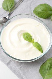 Photo of Tasty yoghurt with basil in bowl on white table, closeup
