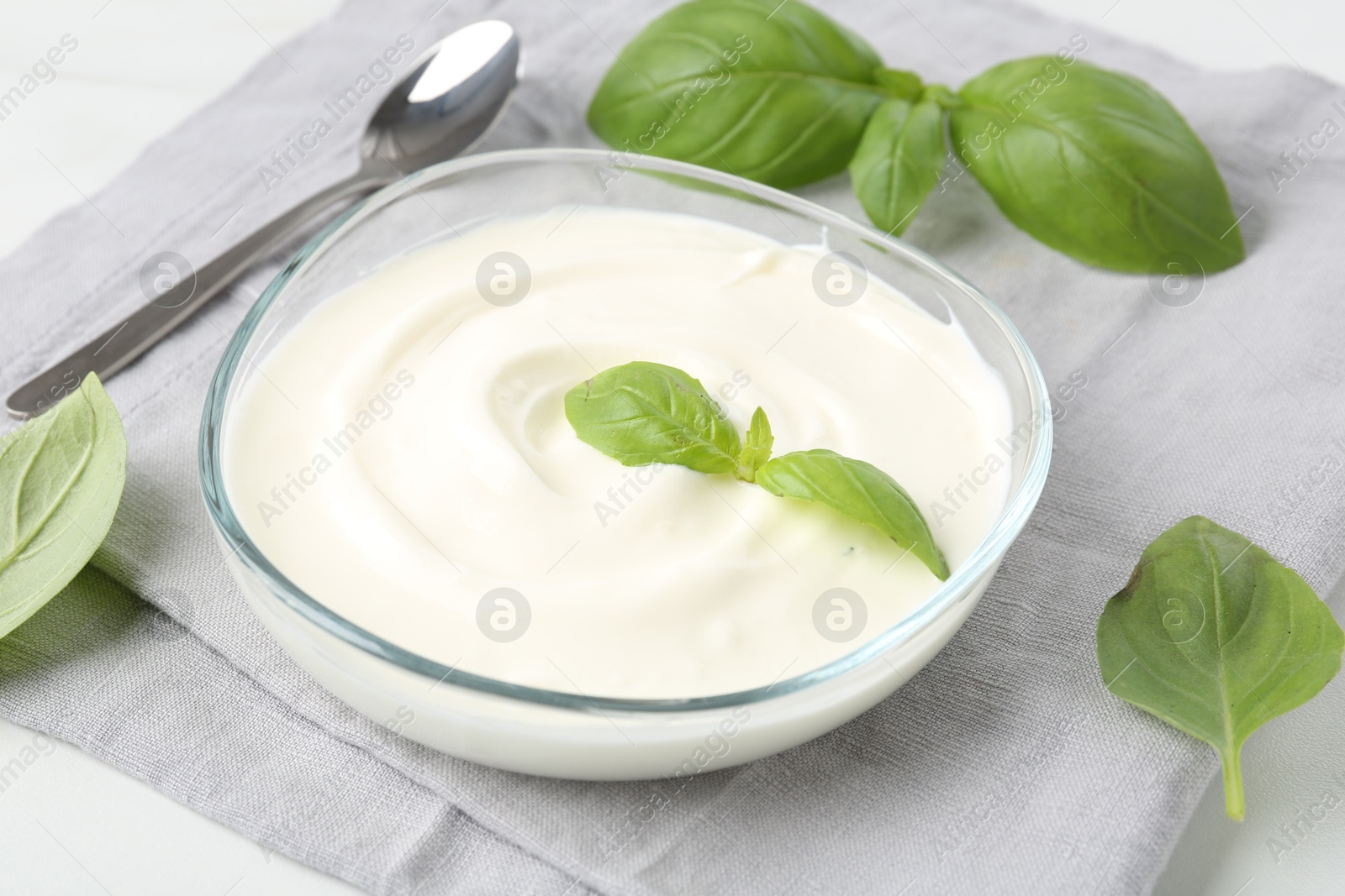 Tasty yoghurt with basil in bowl on white table, closeup Photo of Tasty yoghurt with basil in bowl on white table, closeup