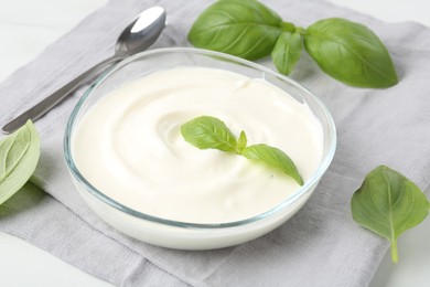 Photo of Tasty yoghurt with basil in bowl on white table, closeup