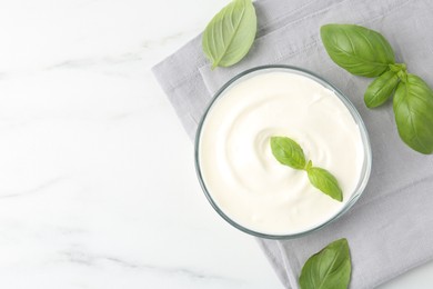 Photo of Tasty yoghurt with basil in bowl on white marble table, flat lay. Space for text