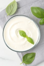Photo of Tasty yoghurt with basil in bowl on white table, flat lay